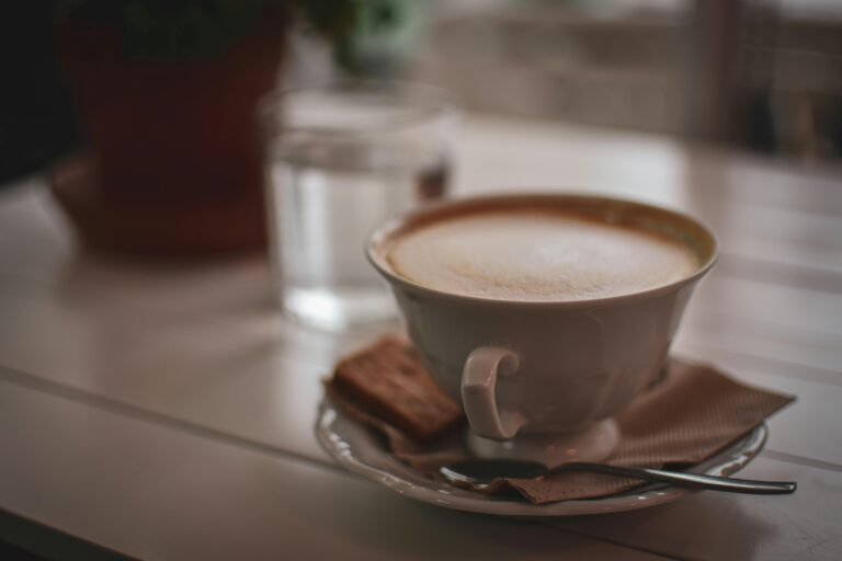 A close-up shot of a cappuccino with a biscuit on a napkin indoors, creating a warm ambiance.