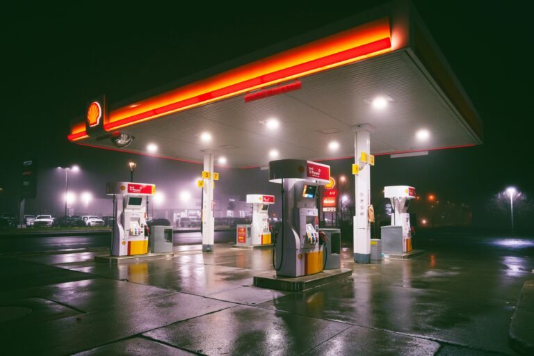 A brightly lit gas station on a rainy night with wet reflections on the ground.